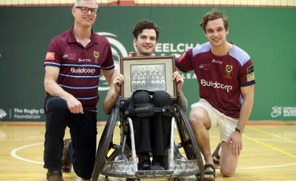 Conor Tweedy, with father Sean and brother Seamus, holds a photo of his grandfather's UQ Rugby premiership-winning side. Credit: Sportography Wheelchair rugby player Conor Tweedy poses with his father and brother on court after a win